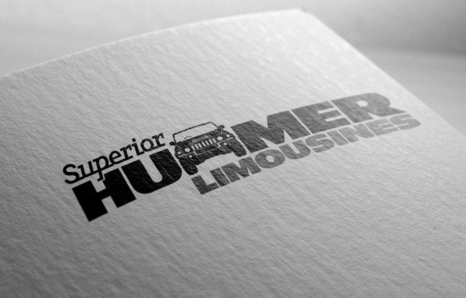 Superior Hummer Limousines letter replacement logo in two colours, black and dark grey on white. "Superior" is set in Javelin a joined-up slab serif italic font inspired 50s automobile badging, positioned above and left of Hummer which is set in all-caps. The first "M" in hummer is replaced by a line drawing of the front elevation of the Hummer. Hummer and Limousines words both set all caps in custom modified Antique Olive Nord font, horizontally extended consistent with Hummer branding. "Superior Hummer" are black, Limousines is dark grey, tucked in below Hummer, aligned right. Brands for New Zealand companies, Christchurch New Zealand.