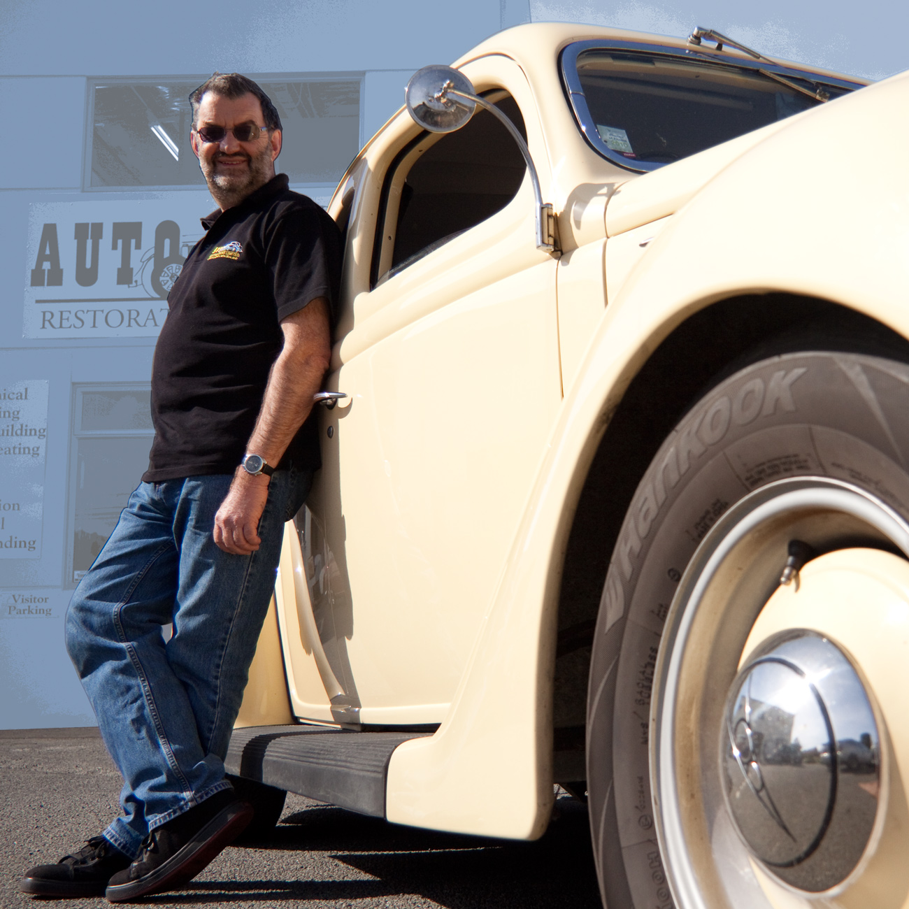 Auto Restorations skilled workforce informal portrait of Allan Wylie, managing director, leaning against his 1938 Ford roadster.