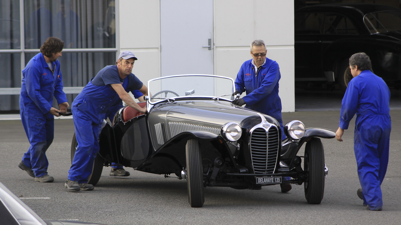 Four of Auto Restorations skilled workforce wheel a custom body Delage Roadster into position in the carpark.