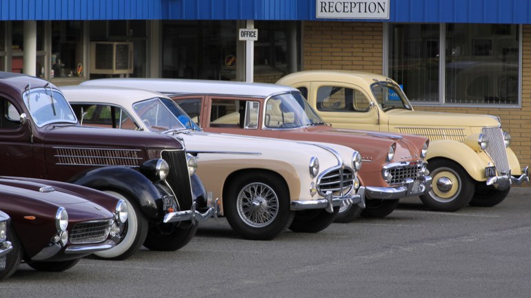 Lineup of classic cars in carpark of Auto Restorations, Stewart Street Christchurch workshop.