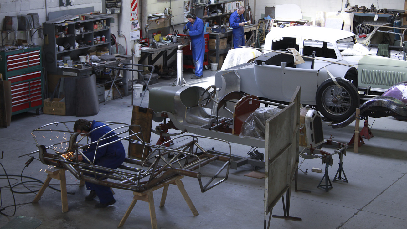 In the foreground Andy Wylie is hand finishing the welding on the bespoke space frame of a 1953 Barchetta recreation “kit” car, in the Custom Coachwork Shop at Auto Restorations.