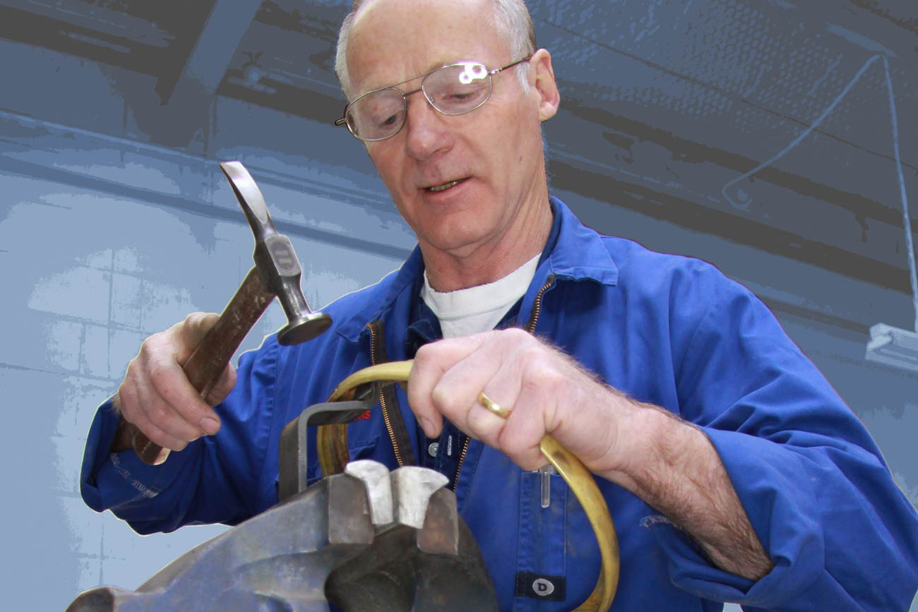 Mike Brosnan hand forms a bespoke brass headlight trim, prior to it being chromed to finish, in the Panel Shop at Auto Restorations.