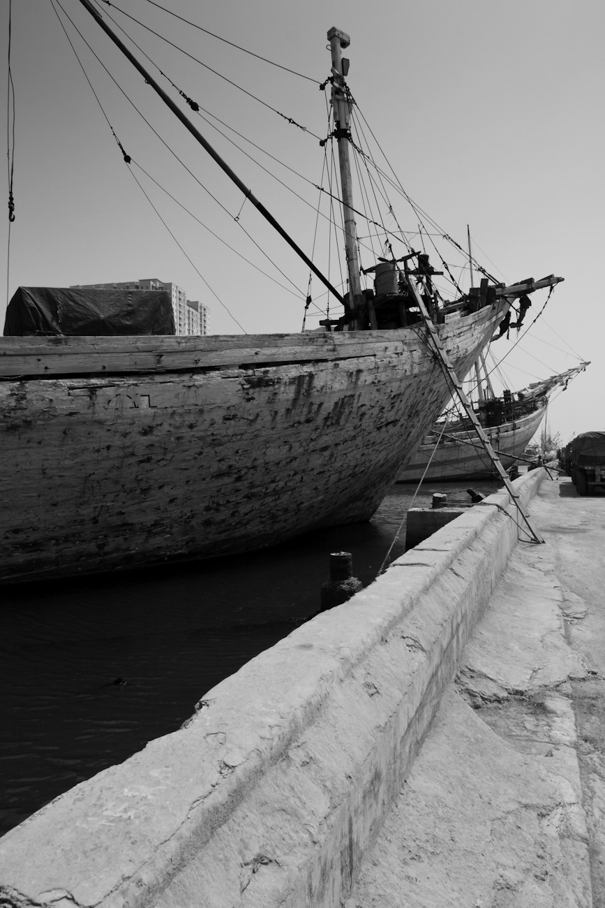 Lambo type motorised Pinisi line up alongside freight trucks at the port of Sunda Kelapa, Jakarta, Indonesia. Pinisi are a traditional Indonesian two to three-masted sailing ship akin to a cutter.