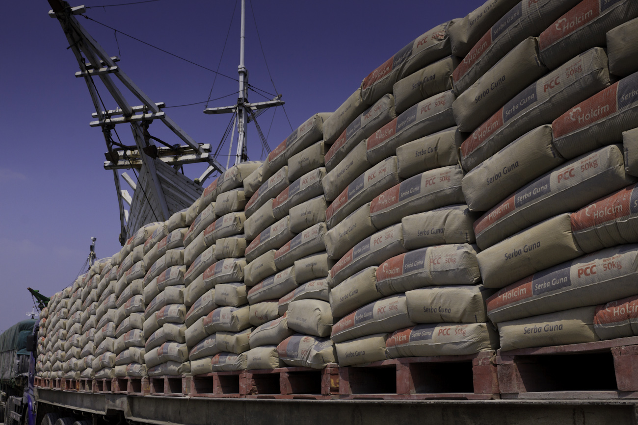 Freight trucks lined up with truckloads of cement, alongside magnificent Makassar schooners called Pinisi at the port of Sunda Kelapa, Jakarta, Indonesia.
