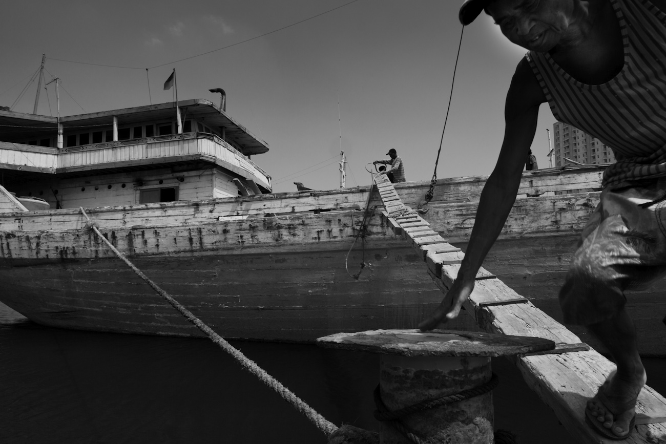 A coolie steps off a wooden cargo boat gangplank. These magnificent Makassar schooners called Pinisiat at the port of Sunda Kelapa, Jakarta, Indonesia.