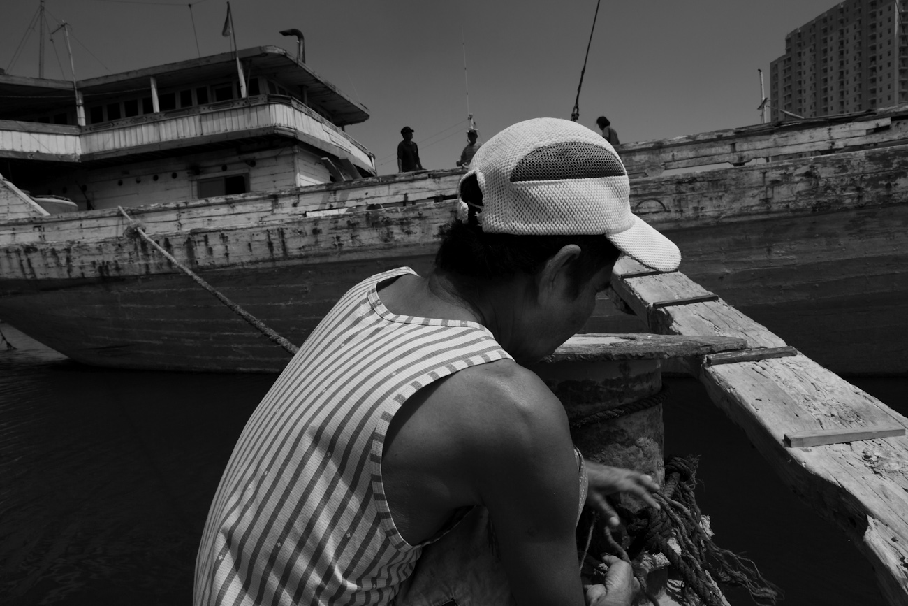 A coolie checks the mooring of a wooden cargo boat. These magnificent Makassar schooners called Pinisiat at the port of Sunda Kelapa, Jakarta, Indonesia.
