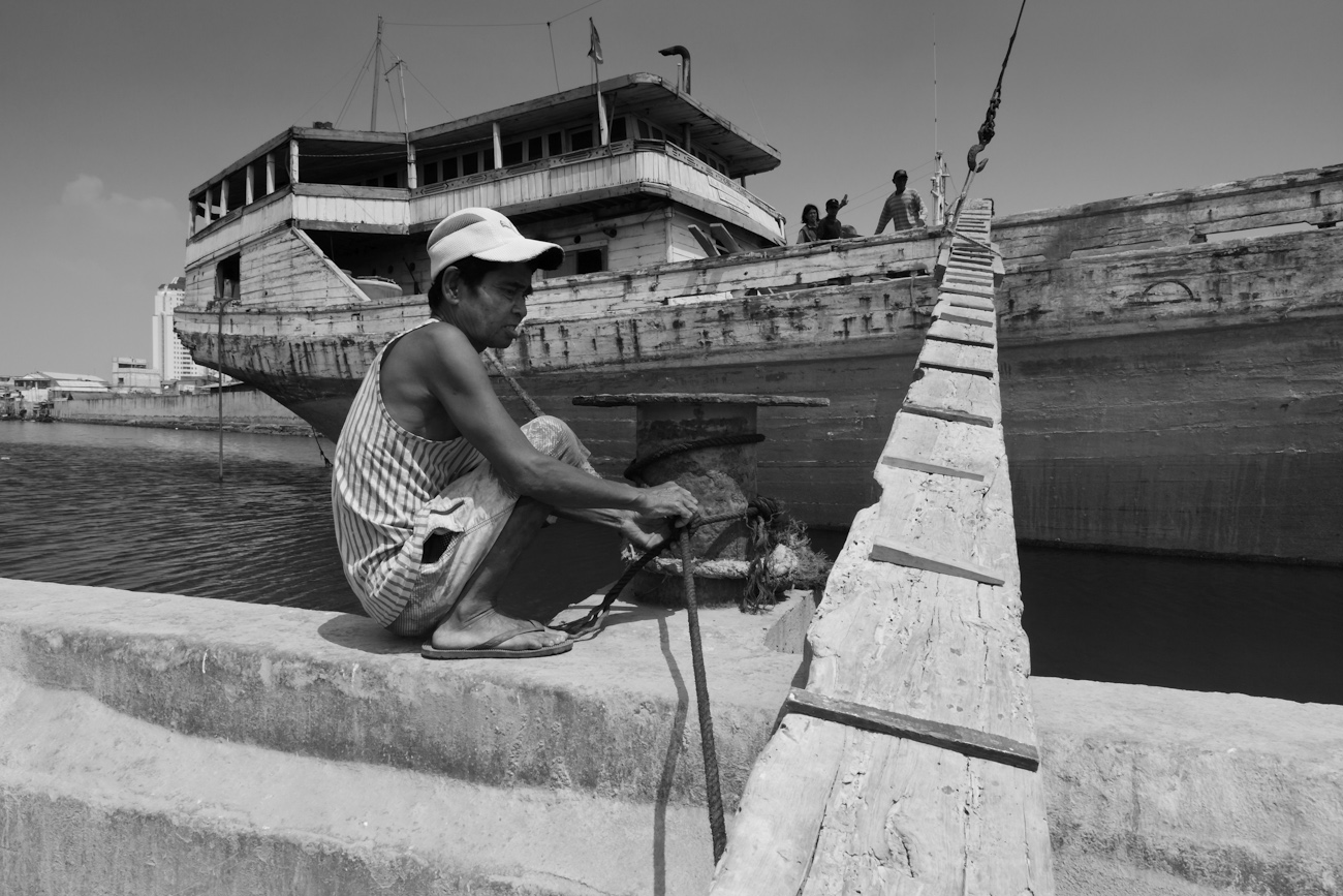 Alongside the gangplank a coolie checks the mooring of a traditional wooden cargo boat. These magnificent Makassar schooners called Pinisi at at the port of Sunda Kelapa, Jakarta, Indonesia.