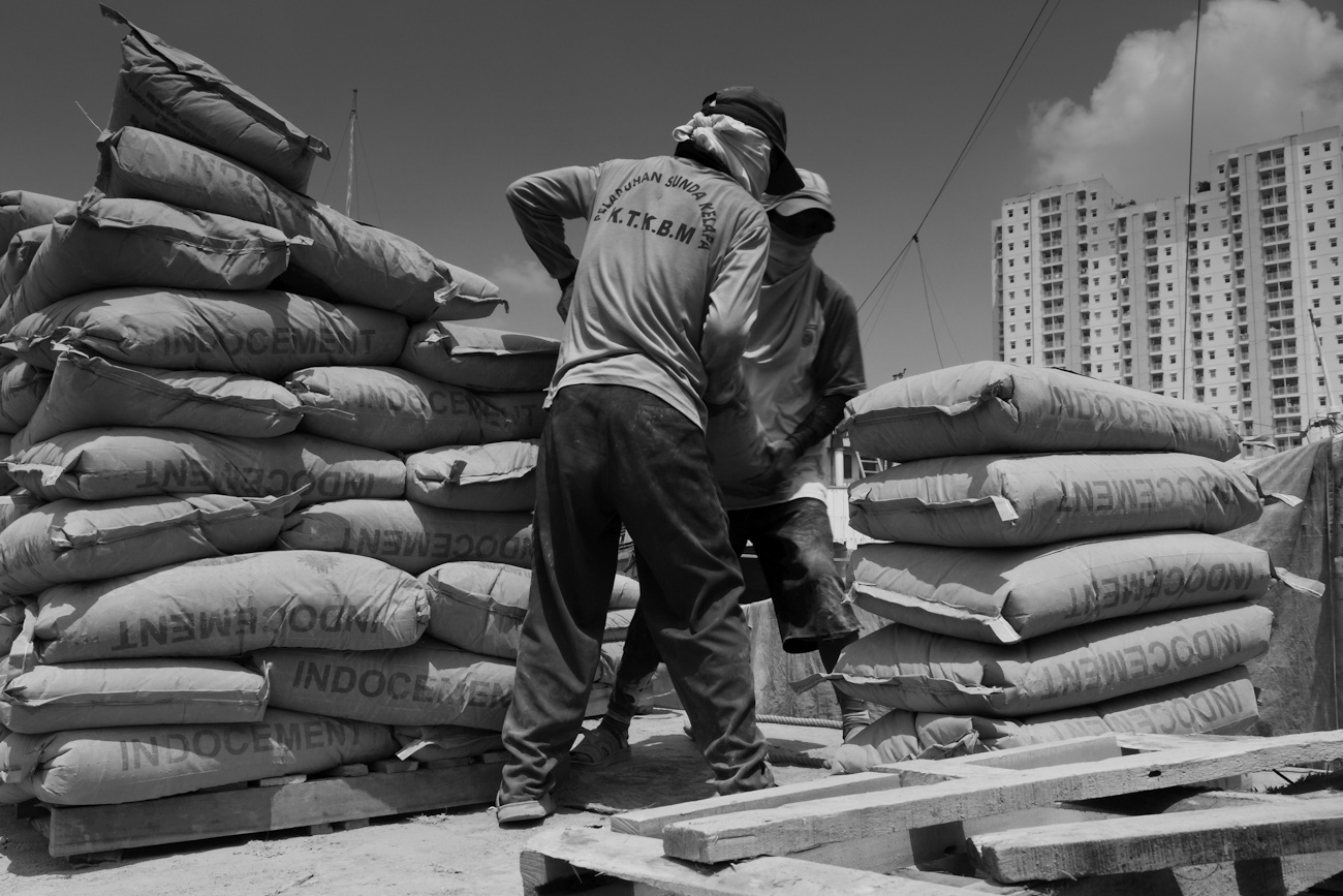 Coolies on the flat deck of a commercial truck alongside a Pinisi freighter load 50 kg bags of Portland Cement onto a wooden pallet to be lifted by crane into the freighter.