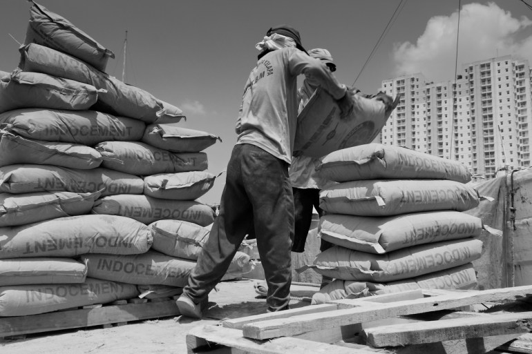 Coolies on the flat deck of a commercial truck alongside a Pinisi freighter load 50 kg bags of Portland Cement onto a wooden pallet to be lifted by crane into the freighter.