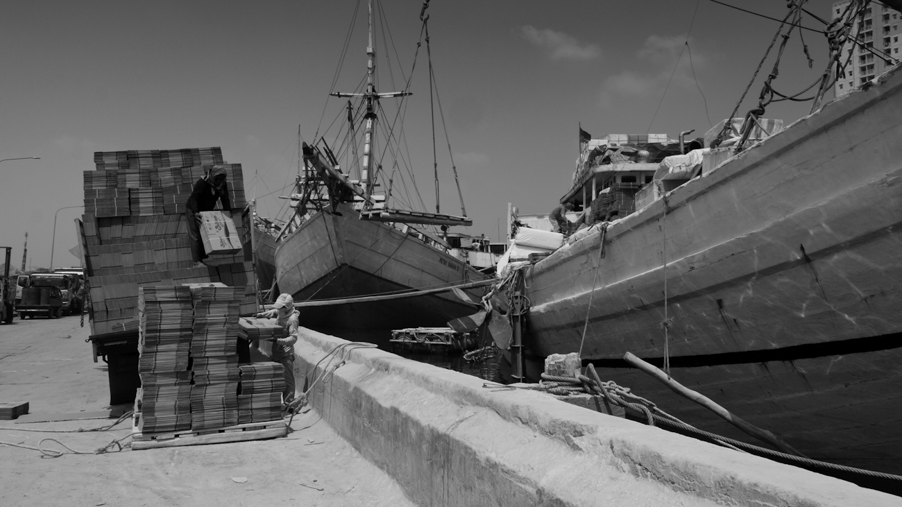Pinisi freighter deck crane lifting platform being hand stacked with flat-packed cardboard boxes prior to transferring to boat.
