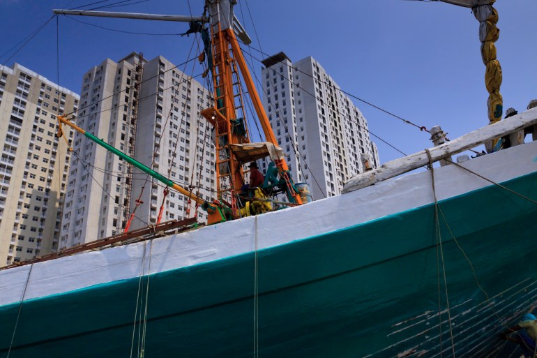 Deck crane operator aboard a motorised Pinisi against a backdrop of towering apartment blocks, port of Sunda Kelapa, old harbour of Jakarta, Indonesia.