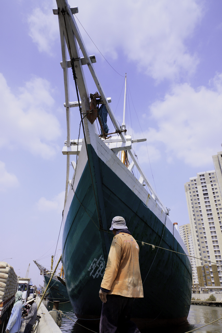 A coolie walks in front of the prow of a magnificent Pinisi traditional Indonesian boat. Port of Sunda Kelapa, old harbour, Jakarta.
