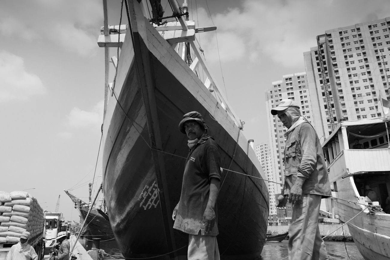 Tow coolies walk in front of the prow of a magnificent Pinisi traditional Indonesian boat. Port of Sunda Kelapa, old harbour, Jakarta.