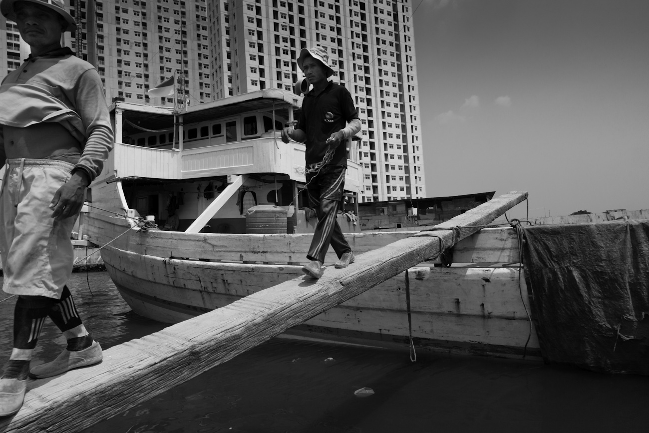 Two coolies walk the gangplank between the deck of a Pinisi and the wharf in the old port of Sunda Kelapa, Jakarta.