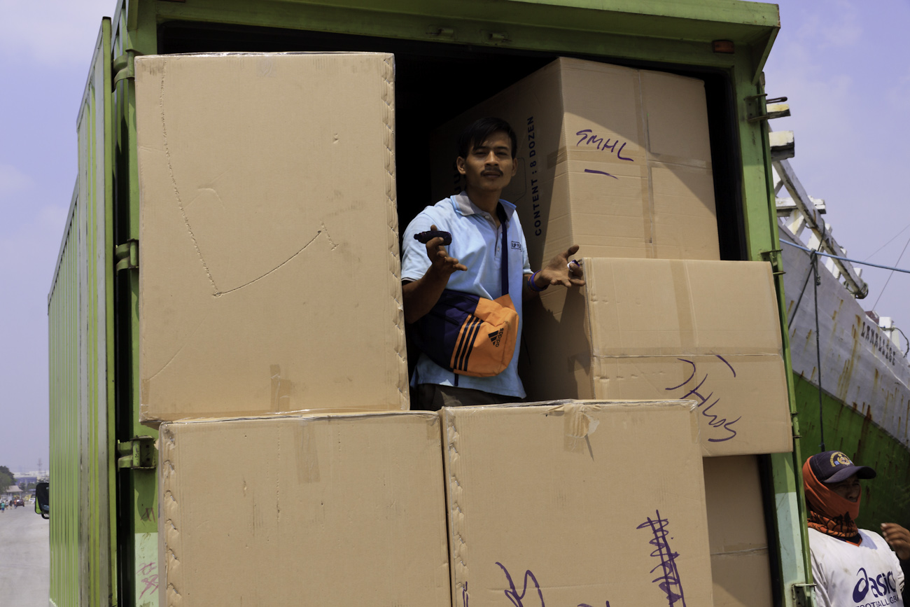 Coolie engaged in cargo operations in the back of a freight truck among large cardboard boxes on the wharf at the old port of Sunda Kelapa, Jakarta, Indonesia..