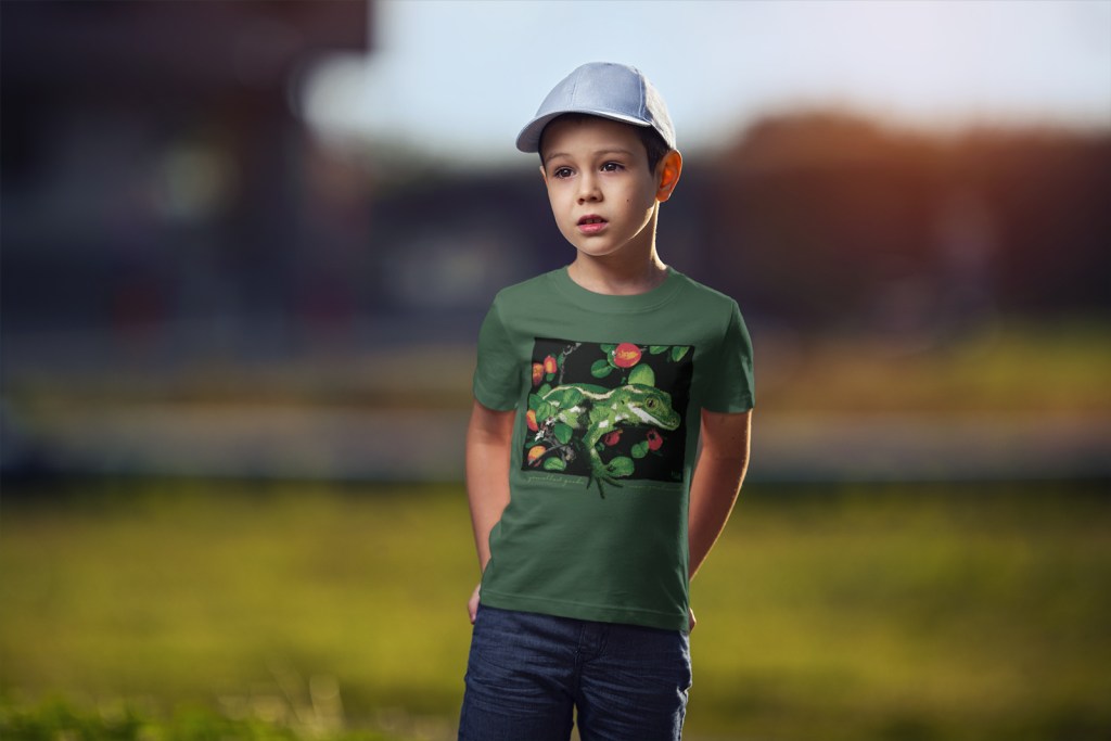 A boy standing in a forest green jewelled gecko New Zealand t-shirt against a blurry background.