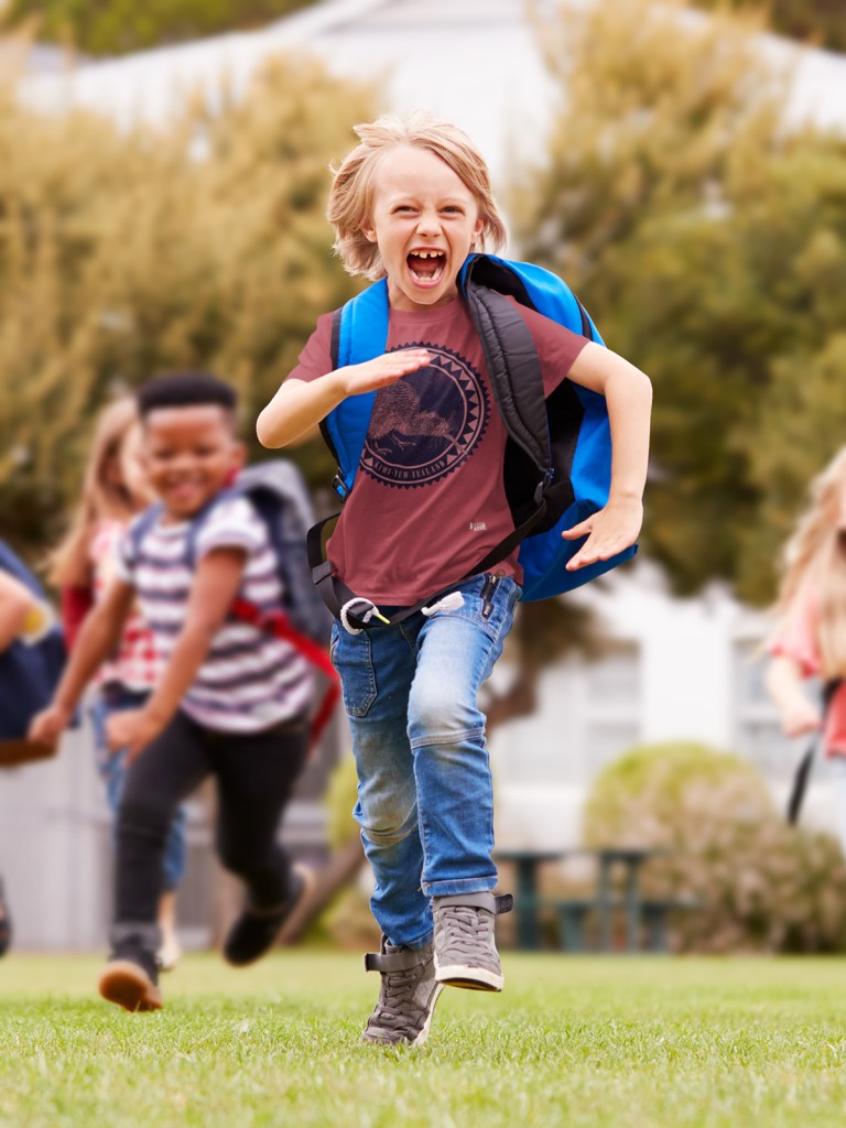 A cheerful young boy running towards the camera in a dark red kiwi New Zealand t-shirt.