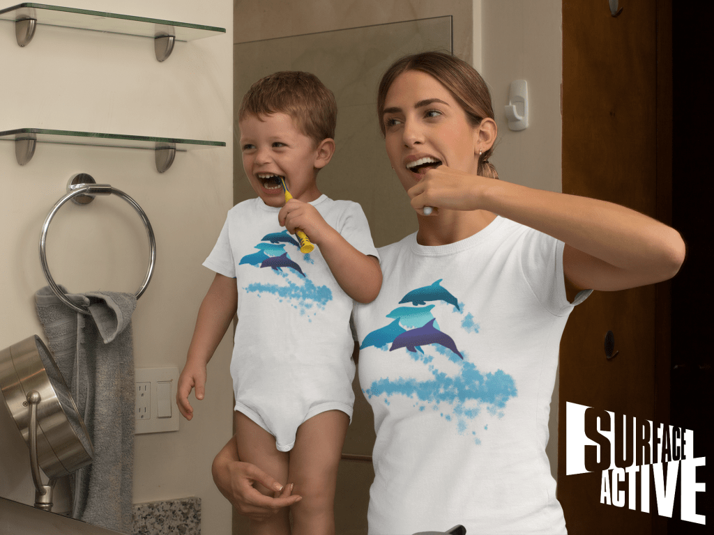 A dolphin onesie on a baby and his mum in a matching dolphin shirt while brushing their teeth