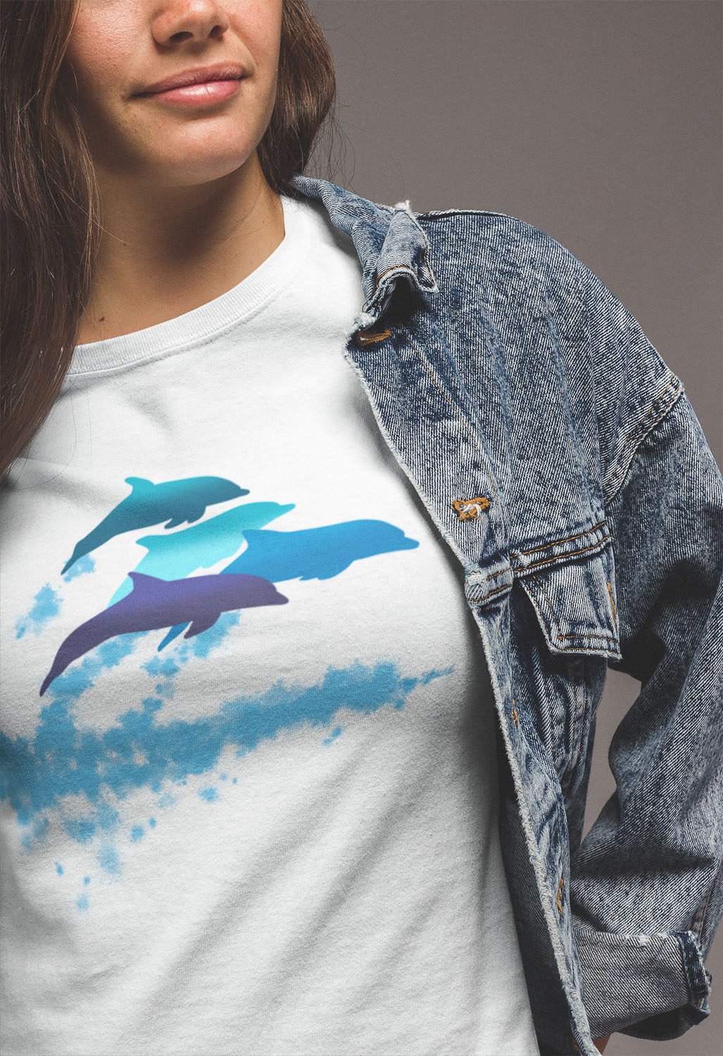 A close-up of a woman wearing a dolphins leaping New Zealand t-shirt under her denim jacket.