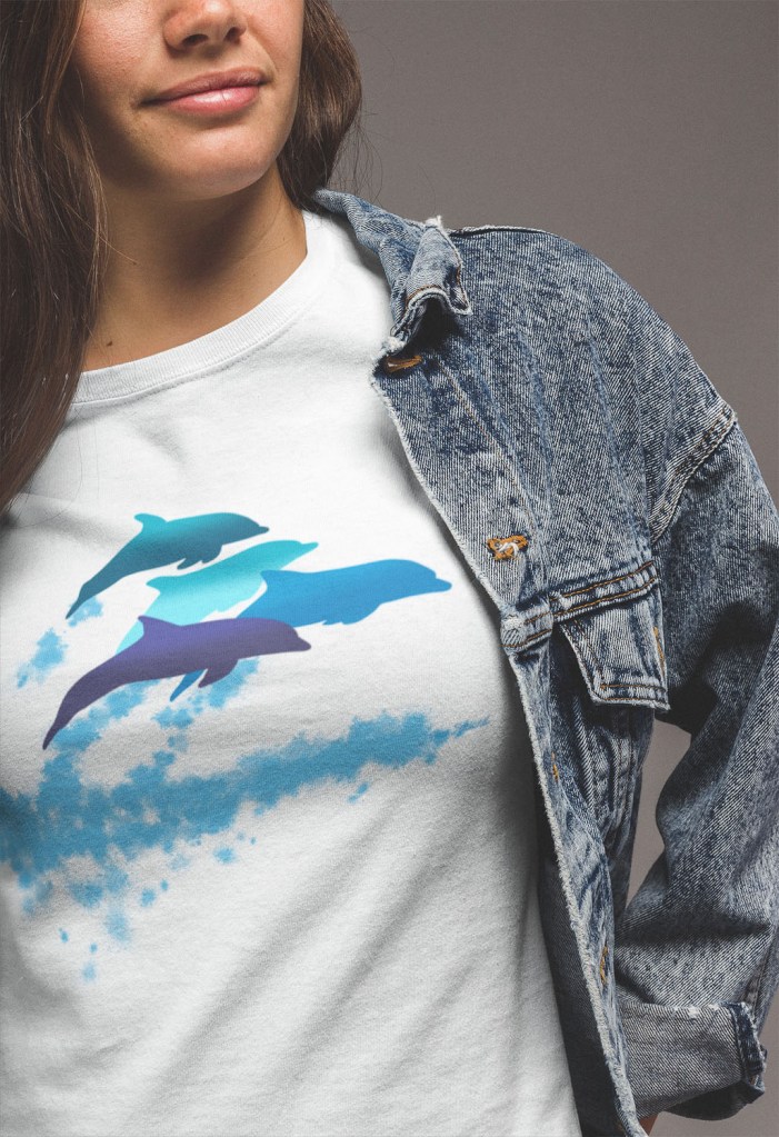 A close-up of a woman wearing a dolphins leaping New Zealand t-shirt under her denim jacket.