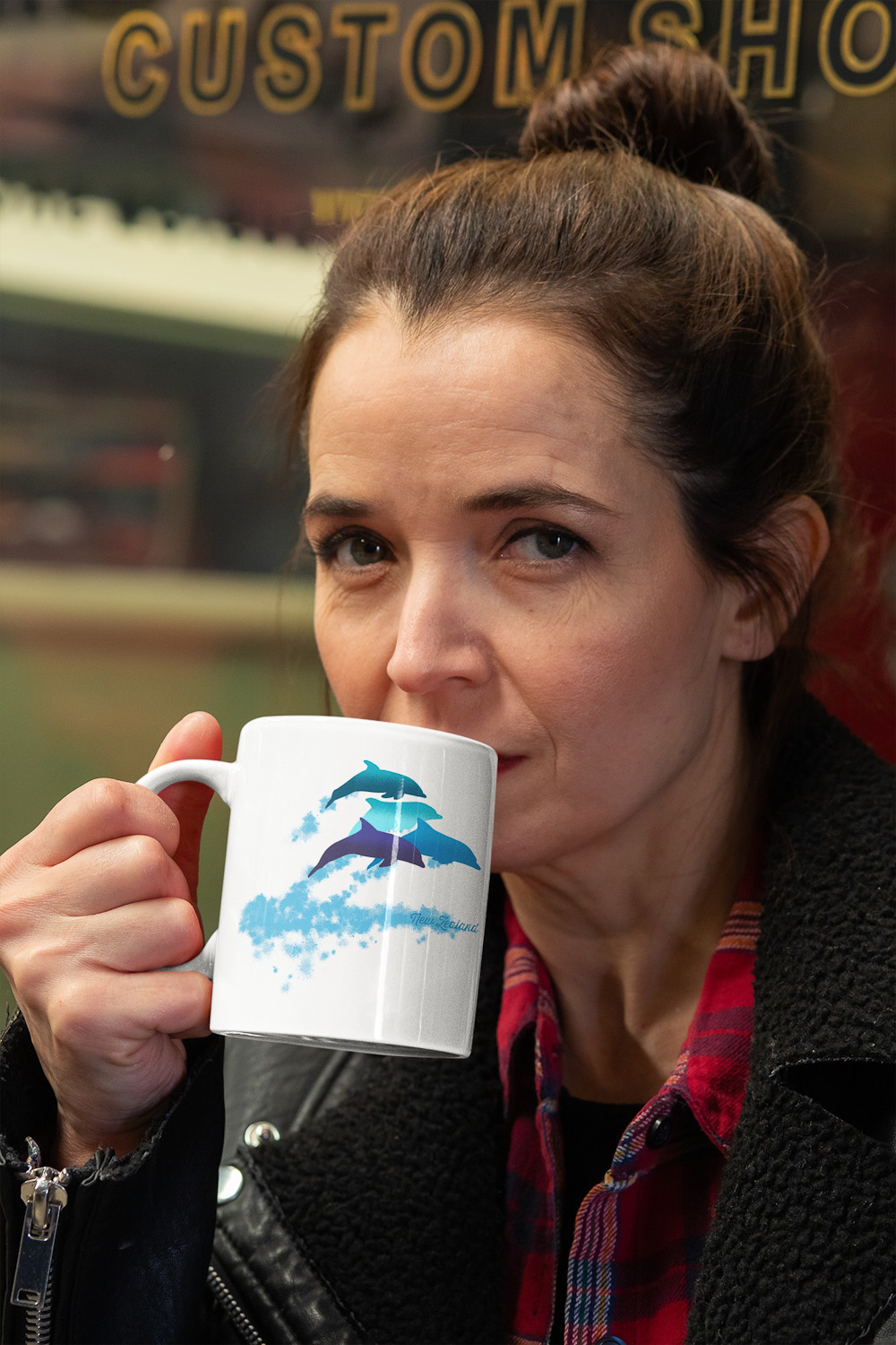 A serious woman drinking from an 11 oz dolphins leaping New Zealand mug while looking at the camera.