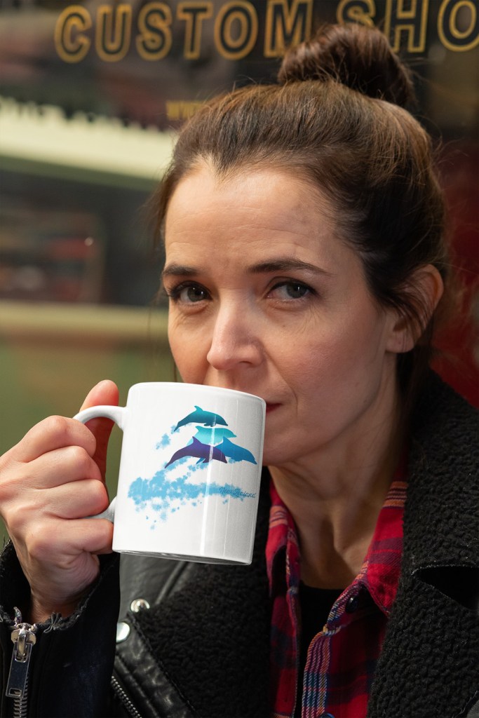 A serious woman drinking from an 11 oz dolphins leaping New Zealand mug while looking at the camera.