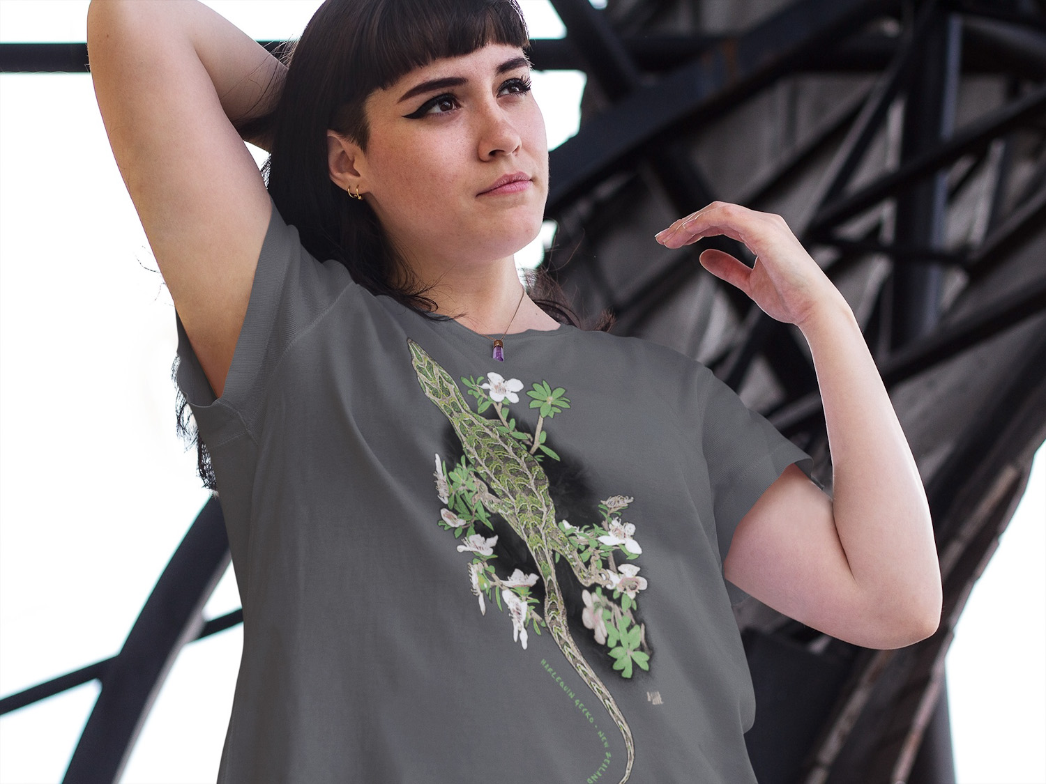 A young woman in an urban area wearing a dark grey t-shirt with a colourful Harlequin Gecko print.