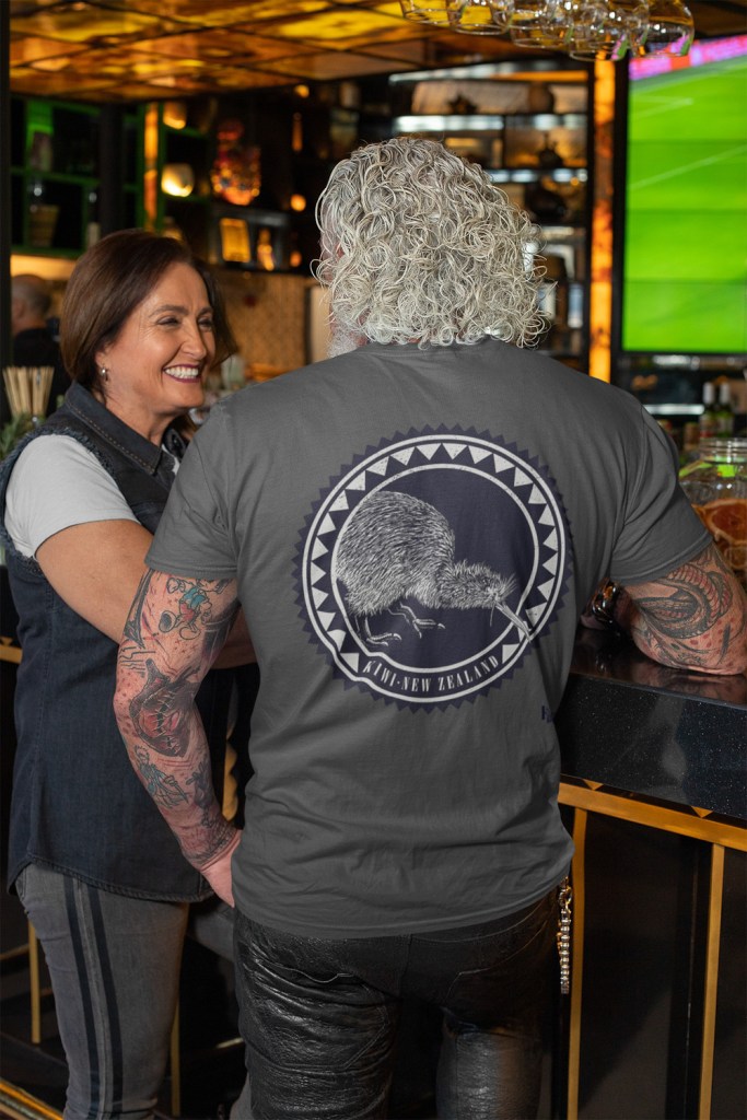 A white-haired man wearing a t-shirt with a dark Kiwi Roundel print, seen from the back.