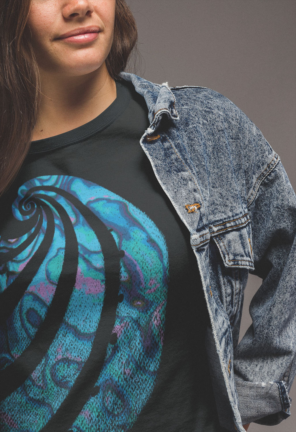 Close up of a woman wearing a black Surface Active paua t-shirt under her denim jacket.