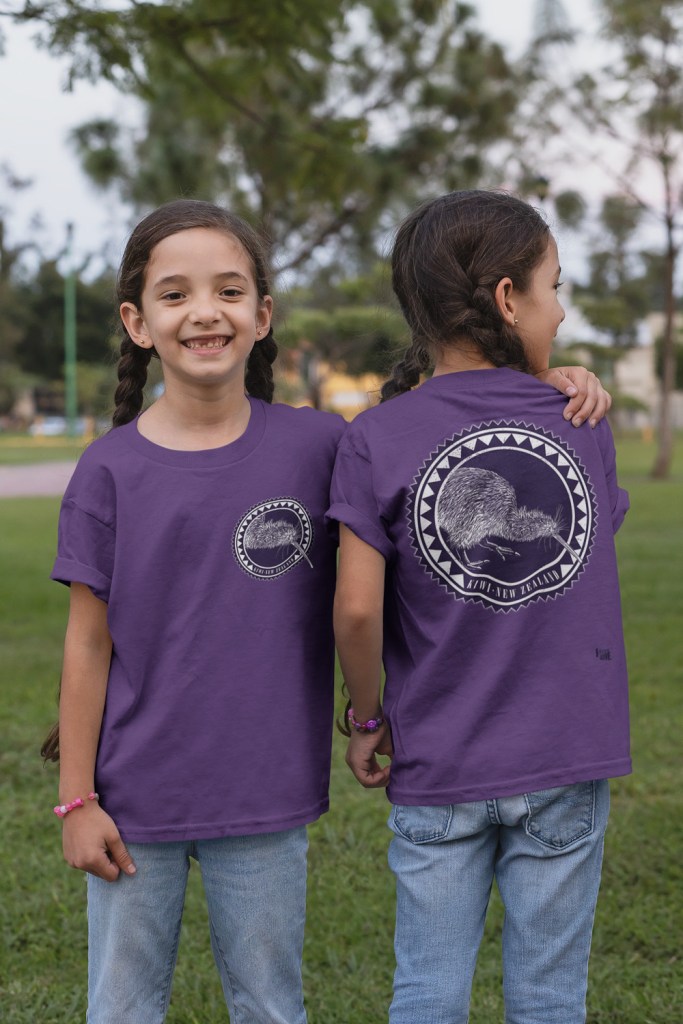 Happy twin girls wearing their matching violet Surface Active Kiwi t-shirts in a park. This variant of the design features large art on the back and a small round kiwi portrait on the front left chest.