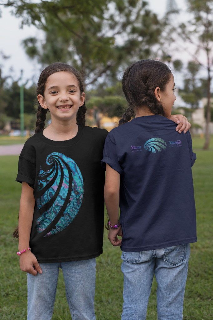 The front and back view of the Paua of the Pacific, Aotearoa, New Zealand children’s t-shirt on black and navy blue tees being worn by happy twin girls in a park.