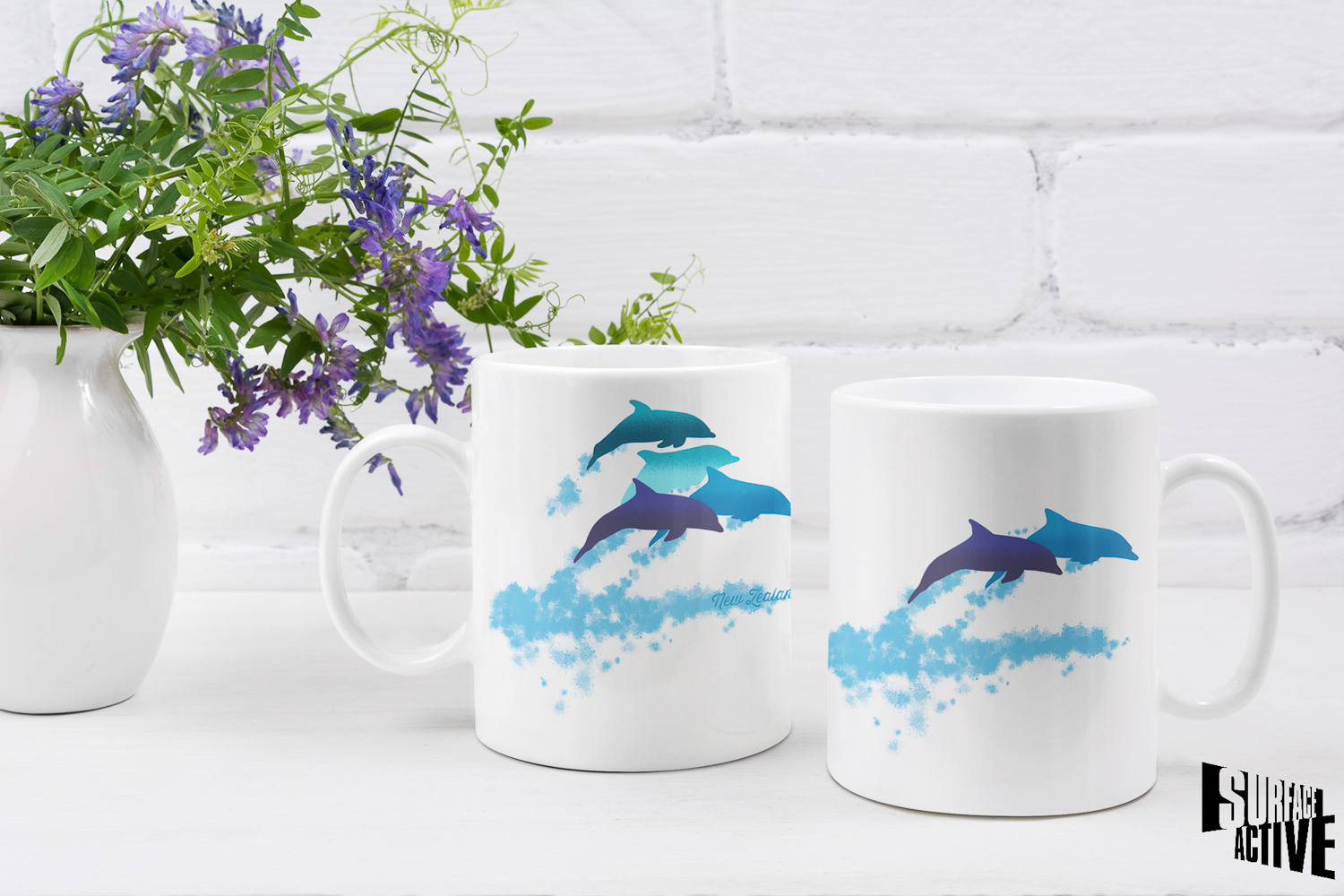 Two 11 oz dolphins leaping New Zealand mugs showing both sides of the two-sided design alongside a floral centrepiece.