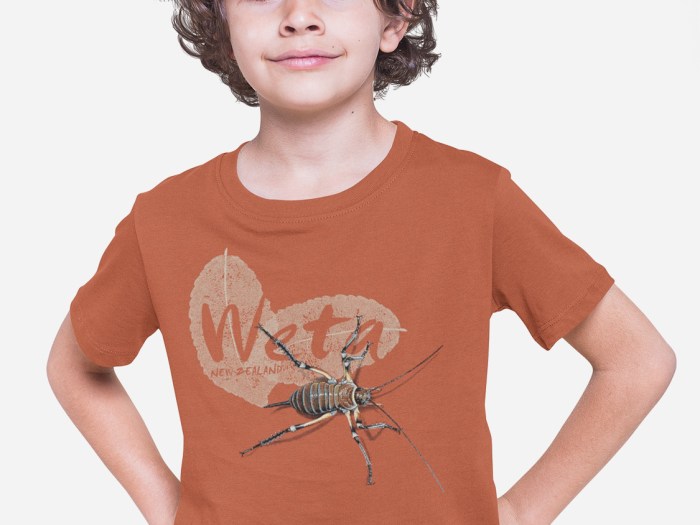 A boy in a studio posing in a terracotta coloured weta New Zealand t-shirt.