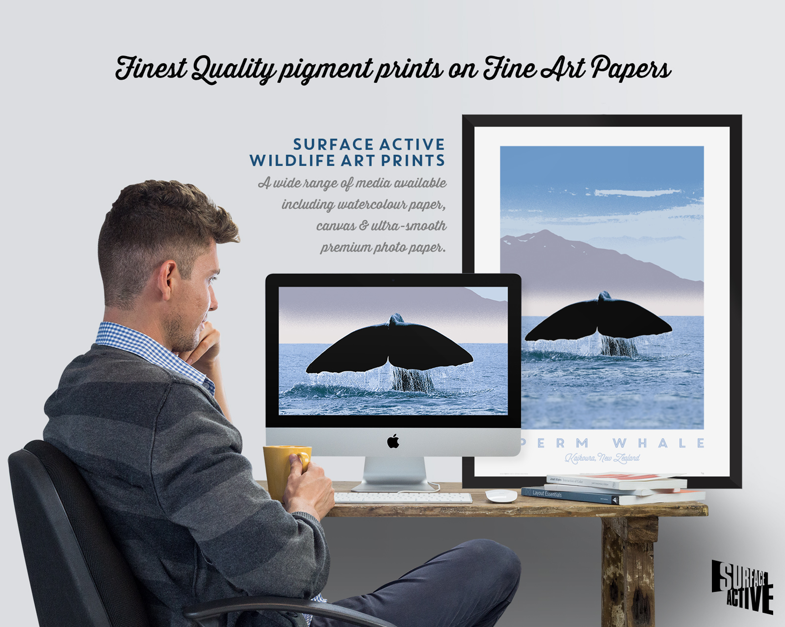 Photo of a young man with a cup of coffee engaged in Surface Active art print production with a sperm whale’s flukes against a Kaikoura coast background on the computer monitor of his iMac and a matching large format framed art print sitting on his desk. The headline against the light grey background of the wall reads “Finest Quality pigment prints on Fine Art Papers. Surface Active Wildlife Art Prints. A wide range of media available including watercolour paper, canvas & ultra-smooth premium photo paper.”