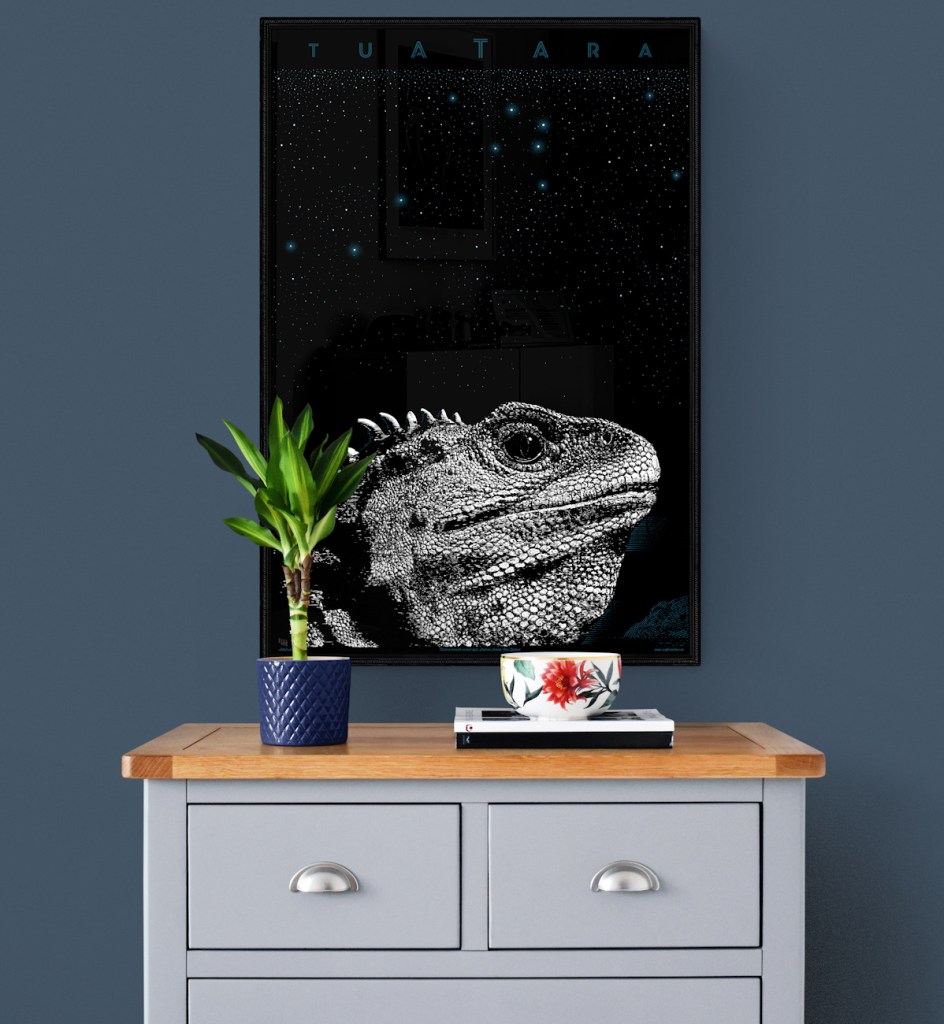 An A1 sized Surface Active Tuatara portrait art print hung behind a grey wood cabinet.
