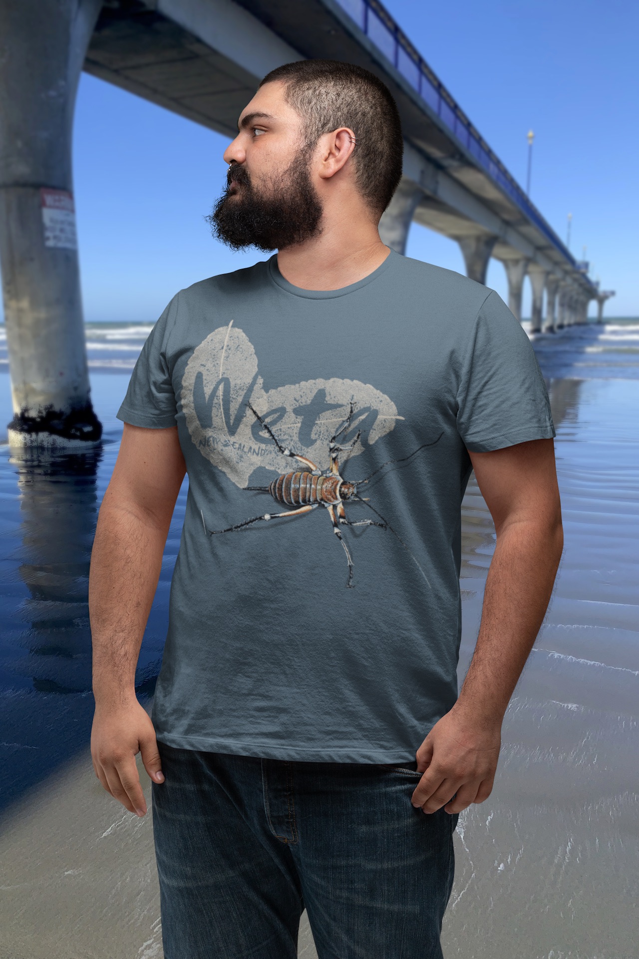 A man wearing a bluestone Giant Weta t-shirt looks sideways beside the newly constructed, concrete and steel New Brighton Pier in Christchurch