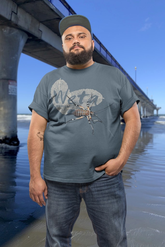 A man wears his bluestone giant weta t-shirt beside New Brighton Pier.