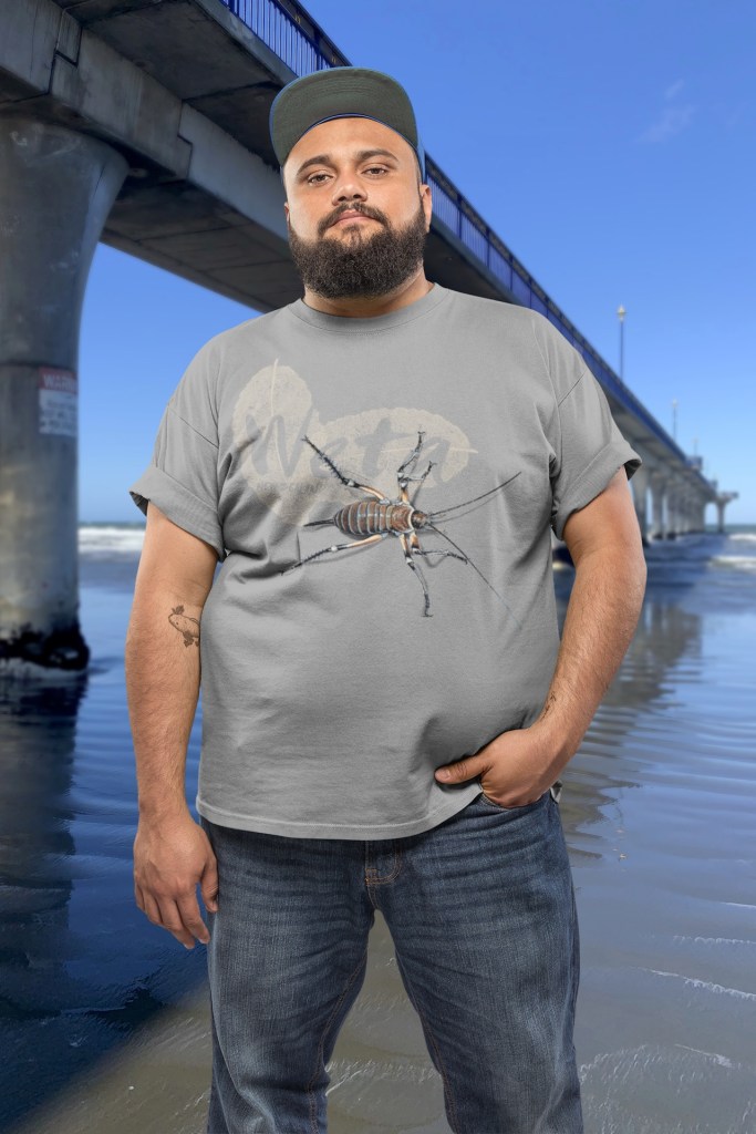 A man wears his grey marle giant weta t-shirt beside New Brighton Pier.
