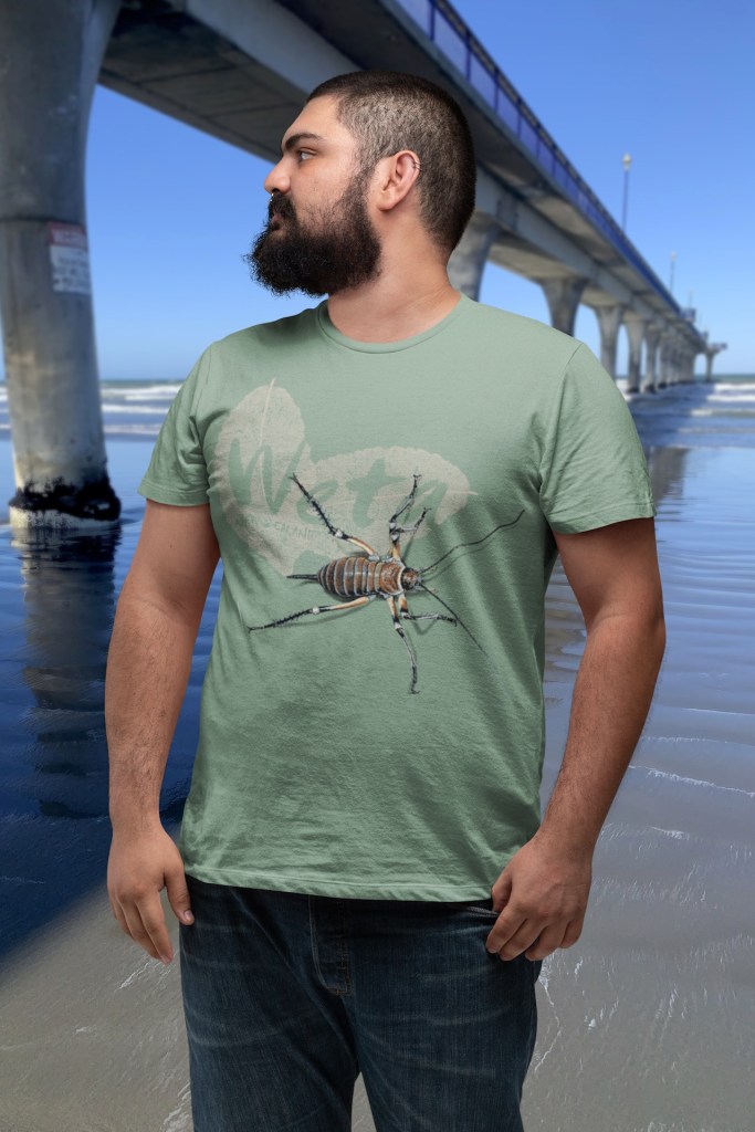 A man looks left while wearing his sage green giant weta t-shirt beside New Brighton Pier.
