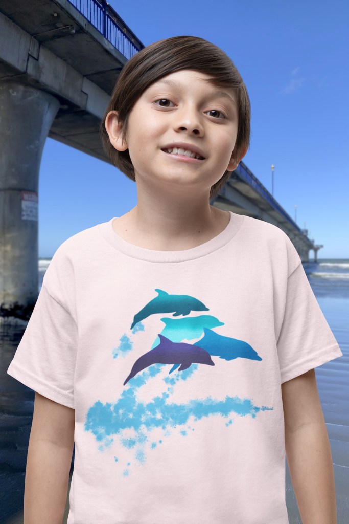 A smiling boy wearing a pink t-shirt with a lively Surface Active “dolphins leaping” print standing beside New Brighton pier.