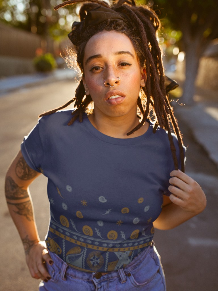 A woman with dreadlocks wearing a navy blue Surface Active tapa t-shirt.