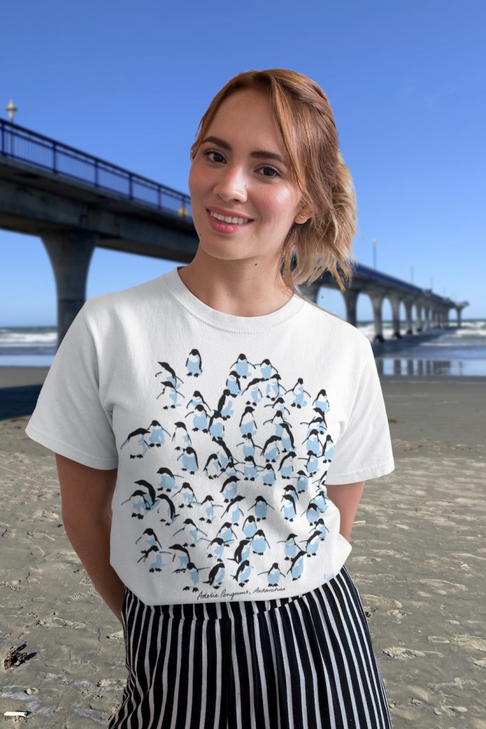 A happy young woman wearing a Surface Active Adelie Penguins, Antarctica t-shirt on New Brighton beach beside the New Brighton pier.