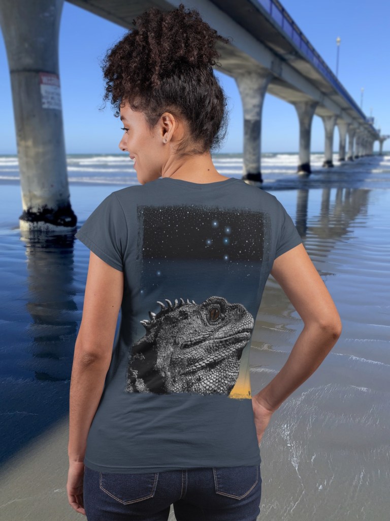 Back view of a happy young woman showing the large art on the back of a Surface Active Tuatara, Stephens Island, New Zealand, t-shirt beside New Brighton Pier.