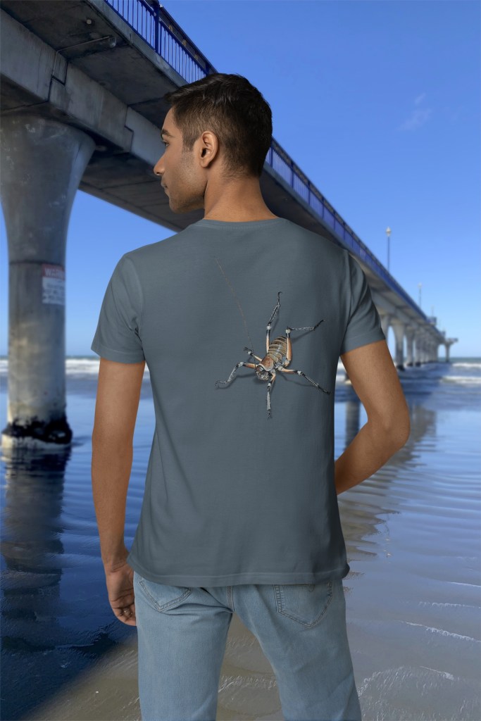 A man showing the back of his Surface Active giant weta t-shirt beside New Brighton Pier.