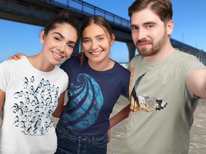 Three friends in Surface Active t-shirts with designs of Adelie penguins, Paua shell, and a red-billed gull at dawn, posing for a selfie at New Brighton Pier.