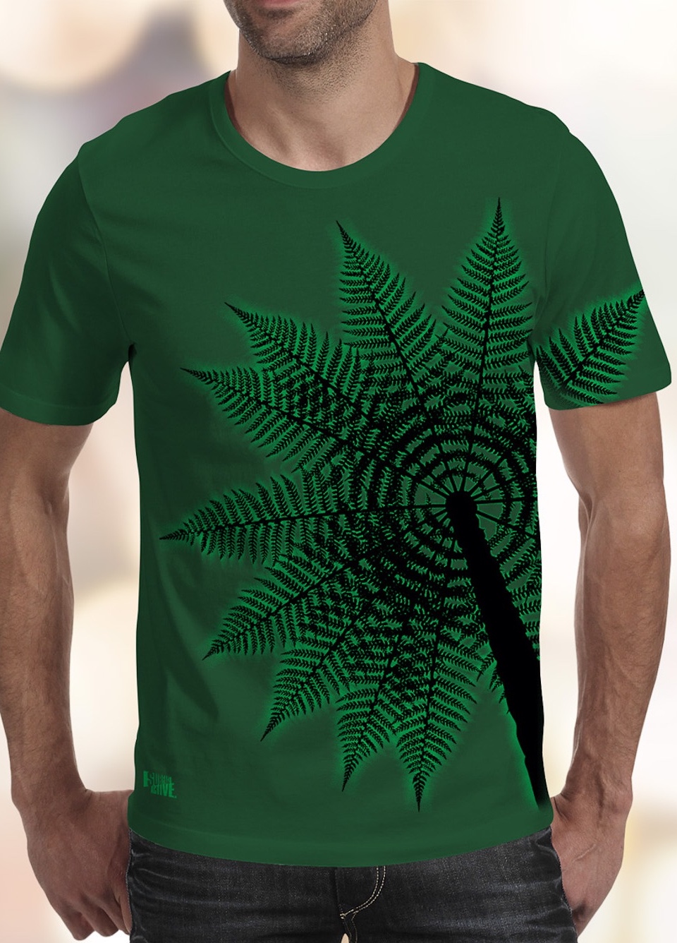 A forest green Surface Active all-over printed Treefern New Zealand t-shirt worn by a young man facing the camera in the studio.