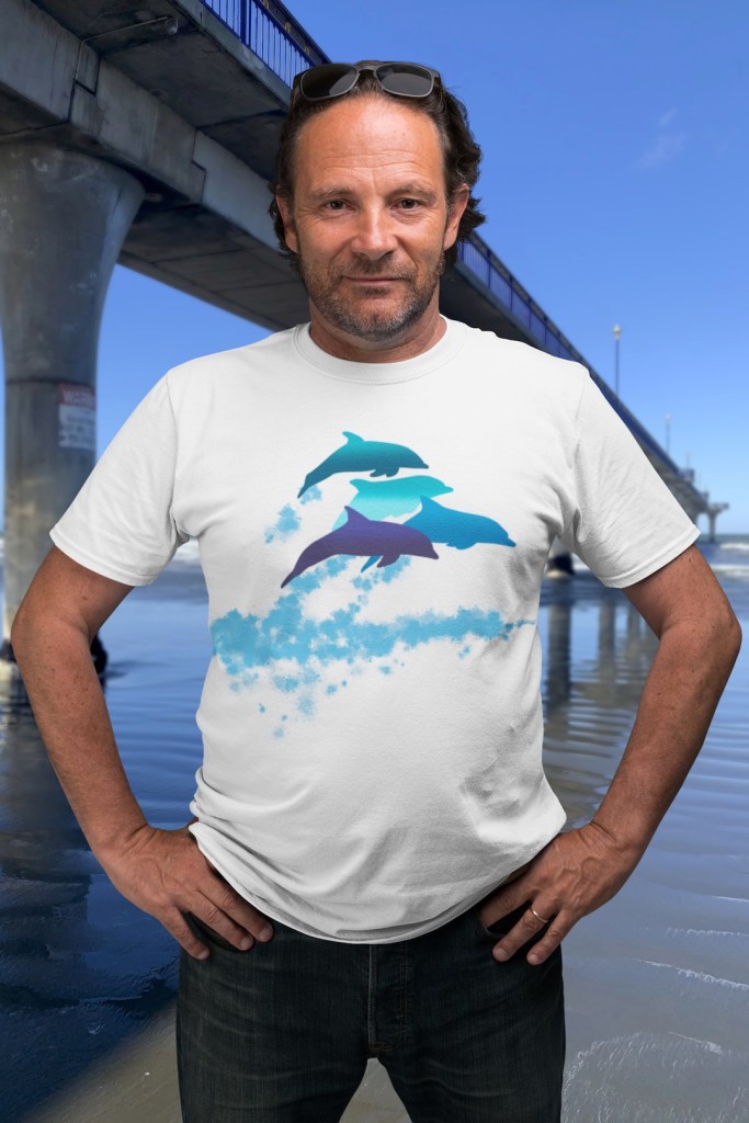 A man with a serious expression wears a white t-shirt with four playful leaping dolphins printed on it, standing beside New Brighton Pier.