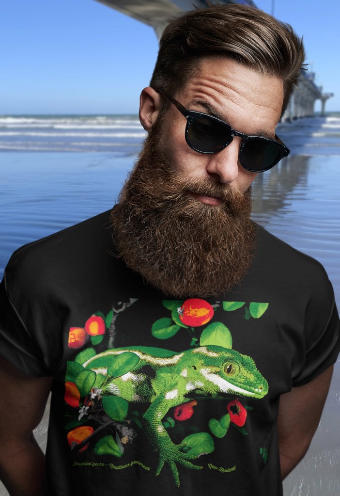 A man wearing a black Surface Active jewelled gecko t-shirt beside New Brighton Pier. The gecko print is a vivid, hand-separated digital illustration of a Jewelled Gecko originally created for screenprinting.
