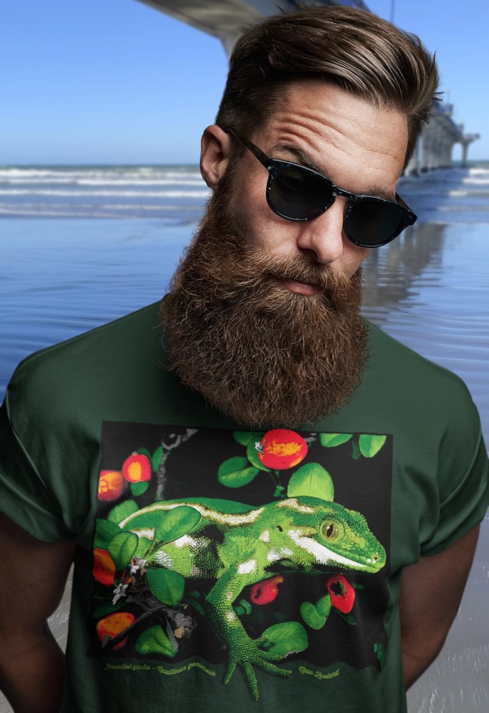 A bearded man in sunglasses wearing a forest green jewelled gecko t-shirt beside New Brighton Pier.