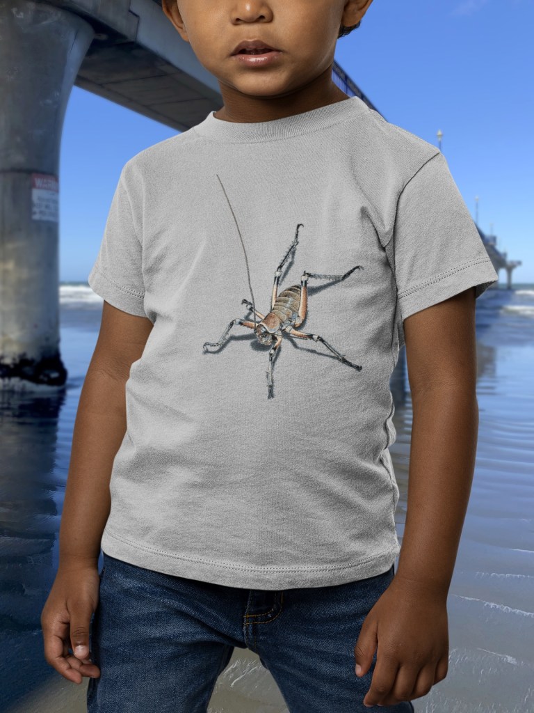 A child wears a grey marle t-shirt with an all-over weta print while standing next to New Brighton Pier, with the ocean in view.